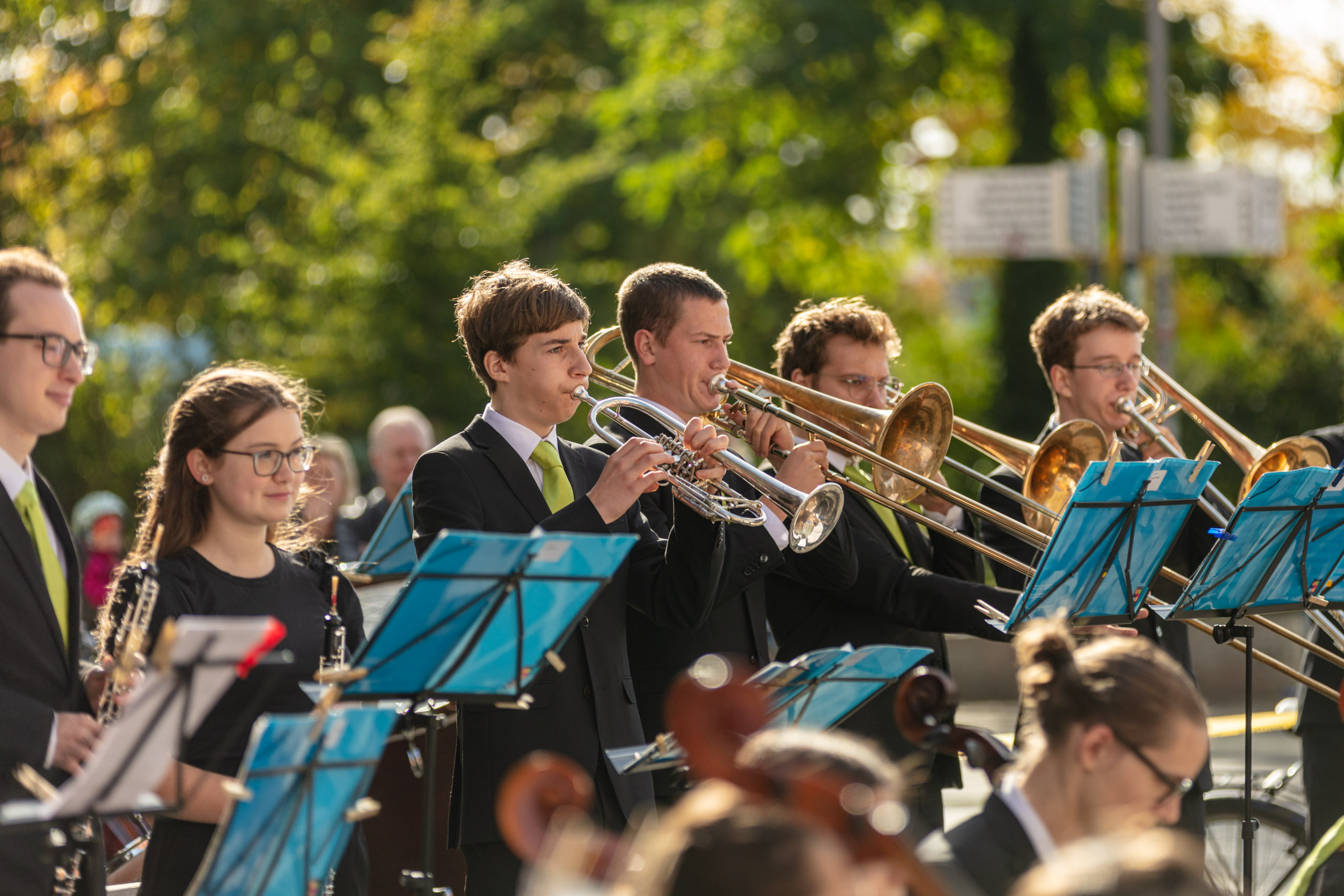 Mitglieder des Jugendsinfonieorchesters spielen draußen verschiedene Blasinstrumente, darunter Oboe, Trompete und Posaune